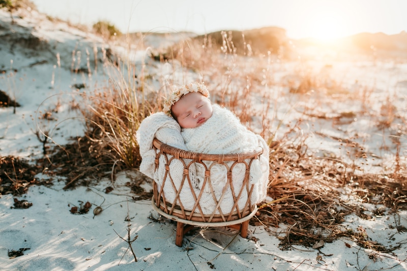Newborn Photographer, a baby sleeps bundled in a basket on the beach