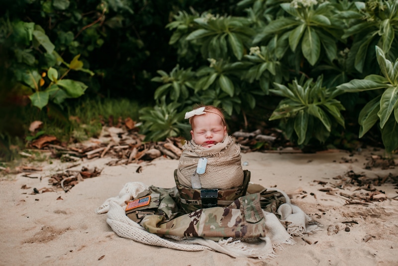 Newborn Photographer, a baby is bundled and sits at the beach before tropical foliage